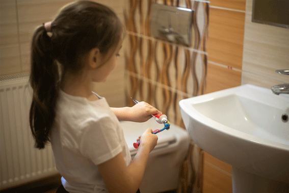niña pequeña echándose pasta de dientes con flúor en el cepillo